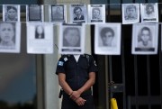 A police officer stands guard outside Guatemala’s Supreme Court, standing between photos of persons who were forcibly disappeared, during a genocide case hearing in Guatemala City, Nov. 25, 2019 (AP photo by Moises Castillo).