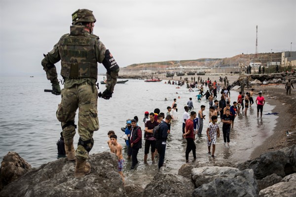 People mainly from Morocco stand on the shore as the Spanish Army cordons off the area at the border of Morocco and Spain, at the Spanish enclave of Ceuta, May 18, 2021 (AP photo by Javier Fergo).