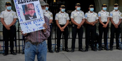 A protester holds a sign with “Resign, Thief” printed over a portrait of Guatemalan President Alejandro Giammattei outside the National Palace in Guatemala City, July 24, 2021 (AP photo by Moises Castillo).