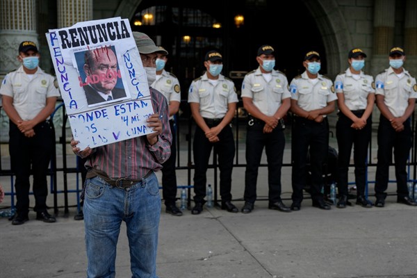 A protester holds a sign with “Resign, Thief” printed over a portrait of Guatemalan President Alejandro Giammattei outside the National Palace in Guatemala City, July 24, 2021 (AP photo by Moises Castillo).