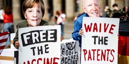 Activists wearing masks depicting German Chancellor Angela Merkel and U.S. President Joe Biden hold signs reading “Free the vaccine” and “Waive the patents,” in front of the Brandenburg Gate, in Berlin, Germany, July 14, 2021 (AP photo by Fabian Sommer).