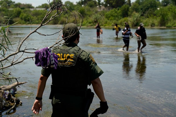 A Border Patrol agent watches as a group of migrants walk across the Rio Grande on their way to turning themselves in upon crossing the U.S.-Mexico border in Del Rio, Texas, June 15, 2021 (AP photo by Eric Gay).
