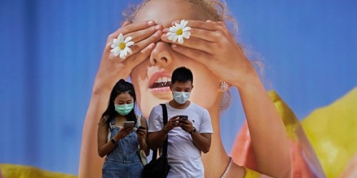 A couple wearing face masks looks at their mobile phones in front of a big poster in Hong Kong, July 27, 2020 (AP photo by Vincent Yu).