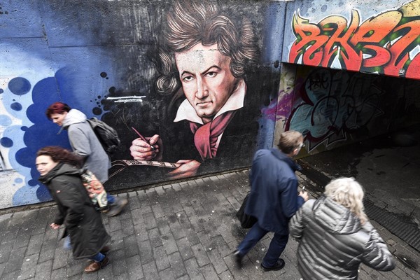 People passing a graffiti mural showing composer Ludwig van Beethoven on a street in Bonn, Germany, Feb. 19, 2020 (AP photo by Martin Meissner).