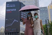 Women walk by an electronic billboard showing China’s GDP index on a commercial office building, in Shanghai, Aug. 24, 2021 (AP photo by Andy Wong).