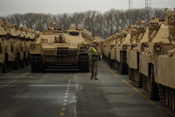A U.S. soldier walks past armored vehicles and tanks as they are unloaded at the port of Antwerp, Belgium, on their way to take part in military exercises in Eastern Europe, Nov. 16, 2020 (AP photo by Francisco Seco).