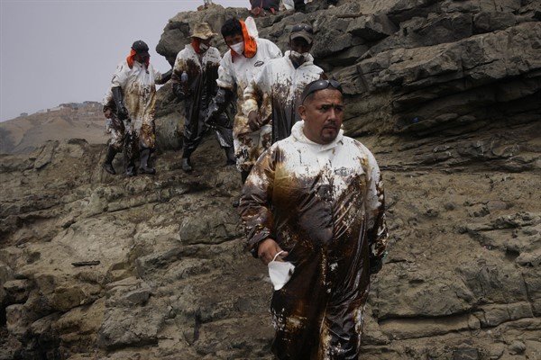Workers are covered in oil after cleaning a spill at Cavero Beach in Ventanilla, a town near Callao, Peru, Jan. 21, 2022 (AP photo by Martin Mejia).