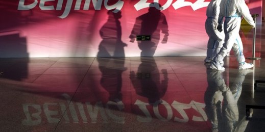 Olympic workers in protective gear walk through the Beijing Capital International Airport as they work to assist passengers ahead of the 2022 Winter Olympics, Beijing, Jan. 31, 2022 (AP photo by Kirsty Wigglesworth).