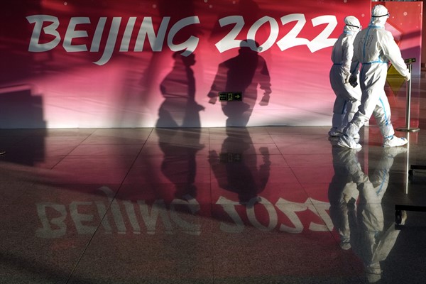 Olympic workers in protective gear walk through the Beijing Capital International Airport as they work to assist passengers ahead of the 2022 Winter Olympics, Beijing, Jan. 31, 2022 (AP photo by Kirsty Wigglesworth).