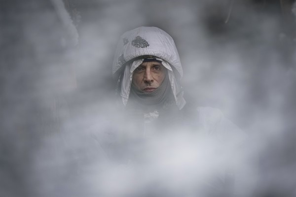 A Ukrainian servicemember, seen through a camouflage mesh, stands at a frontline position in the Luhansk region, eastern Ukraine, Jan. 29, 2022 (AP photo by Vadim Ghirda).