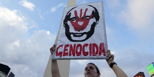 A woman holds a sign with the face of Russian President Vladimir Putin and the word “Genocida,” or committer of genocide, during a protest against the Russian invasion of Ukraine, Buenos Aires, Argentina, March 6, 2022 (AP photo by Natacha Pisarenko).