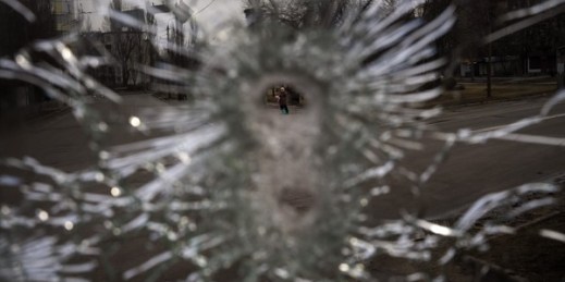 A man is seen through a bullet hole of a machine-gunned bus that Ukrainian authorities say was ambushed on Feb. 26 by Russian “saboteurs,” Kyiv, Ukraine, March 4, 2022 (AP photo by Emilio Morenatti).