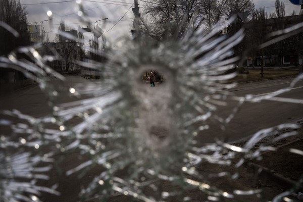 A man is seen through a bullet hole of a machine-gunned bus that Ukrainian authorities say was ambushed on Feb. 26 by Russian “saboteurs,” Kyiv, Ukraine, March 4, 2022 (AP photo by Emilio Morenatti).