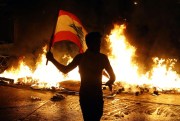 An anti-government protester waves a Lebanese flag in front of a burning barricade on a road leading to the parliament building, Beirut, Lebanon, Nov. 13, 2019 (AP photo by Bilal Hussein).