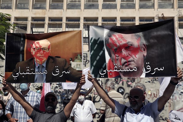 Bank customers hold up a defaced poster of Central Bank chief Riad Salameh, right, reading, “Stole my future,” in Arabic, during a protest in front of the Central Bank, Beirut, Lebanon, Oct. 6, 2021 (AP photo by Bilal Hussein).