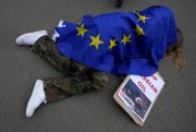A protester covered by an EU flag takes part in a demonstration to call on the European Union to stop buying Russian oil and gas, outside EU headquarters in Brussels, April 29, 2022 (AP photo by Virginia Mayo).