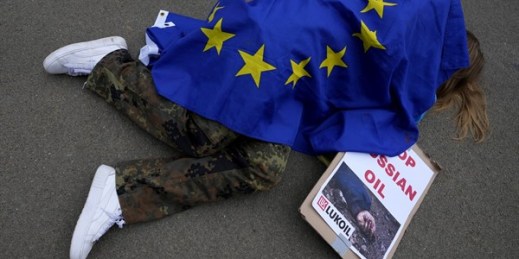 A protester covered by an EU flag takes part in a demonstration to call on the European Union to stop buying Russian oil and gas, outside EU headquarters in Brussels, April 29, 2022 (AP photo by Virginia Mayo).