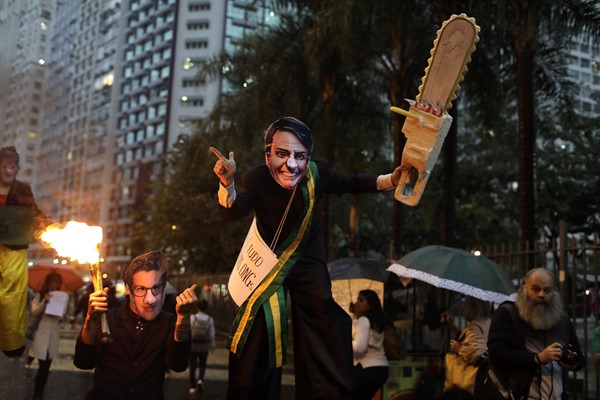 A demonstrator wearing a mask of Brazilian President Jair Bolsonaro and brandishing a fake chainsaw marches in defense of the Amazon in Rio de Janeiro, Brazil, Sept. 5, 2019 (AP photo by Silvia Izquierdo).