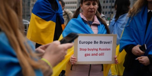 A protester holds a sign as she takes part in a demonstration to call on the European Union to stop buying Russian oil and gas, outside EU headquarters in Brussels, April 29, 2022 (AP photo by Virginia Mayo).