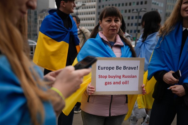 A protester holds a sign as she takes part in a demonstration to call on the European Union to stop buying Russian oil and gas, outside EU headquarters in Brussels, April 29, 2022 (AP photo by Virginia Mayo).