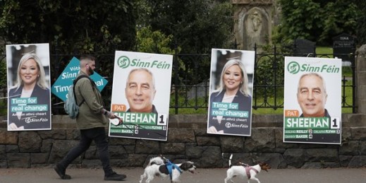 A man walks his dogs past election posters in West Belfast, Northern Ireland, May 5, 2022 (AP photo by Peter Morrison).