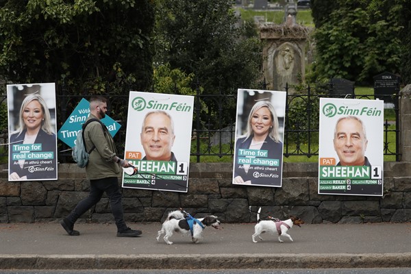 A man walks his dogs past election posters in West Belfast, Northern Ireland, May 5, 2022 (AP photo by Peter Morrison).