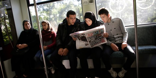 Syrian refugees sit in a train and read a local newspaper with special pages in Arabic for refugees, Berlin, Sept. 9, 2015.