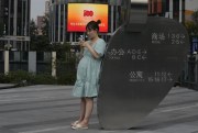 A pregnant woman looks at her smartphone near a logo marking the 100th anniversary of the founding of the ruling Communist Party in Beijing, July 8, 2021 (AP photo by Ng Han Guan).