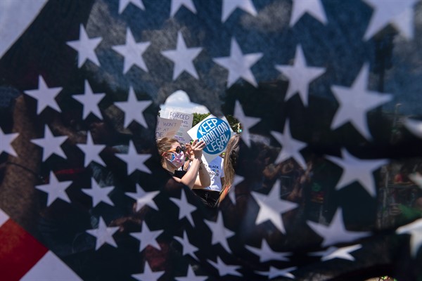 Abortion rights activists are seen through a hole in an American flag as they protest outside the Supreme Court in Washington, June 25, 2022 (AP photo by Jose Luis Magana).