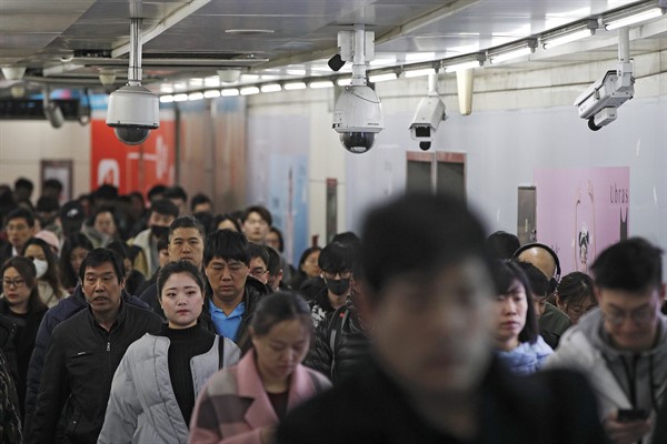 Commuters walk by surveillance cameras installed at a walkway in between two subway stations in Beijing, Feb. 26, 2019 (AP photo by Andy Wong).