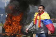 A man draped with an Ecuadorean flag protests next to a burning barricade, Santa Rosa, Ecuador, June 14, 2022 (AP photo by Dolores Ochoa).