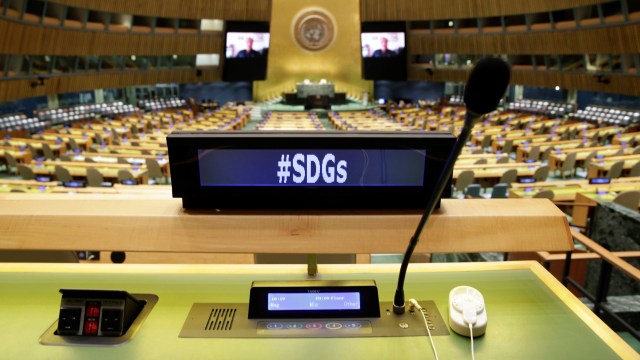 A desk screen displays “#SDGs” in the U.N. General Assembly Hall.