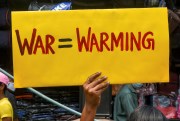 An activist holds a sign reading "war=warming."