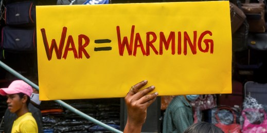 An activist holds a sign reading "war=warming."