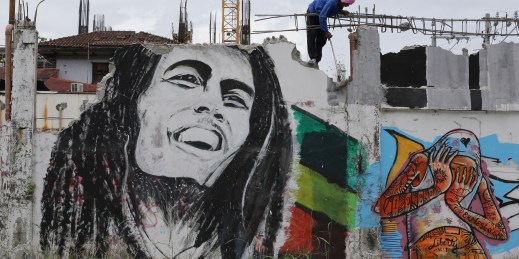 A Filipino worker tears down a wall showing a mural painting of Bob Marley.