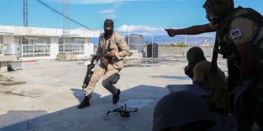 A Haitian police officer runs to take cover with Kenyan police members of a U.N.-backed multinational force.