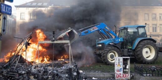 A farmer in a tractor near a burning barricade.
